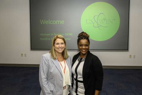 Pam Cowen and Minneva Taltoan pose for the camera together. A U.S. WIN welcome banner is shown behind them.